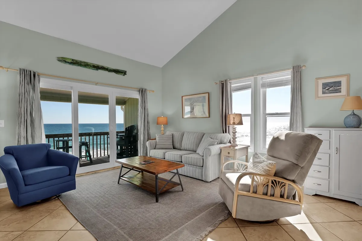 A comfortable interior seating area with large windows framing a panoramic ocean view. The space features plush chairs and a coffee table, suggesting a cozy spot to relax indoors while still enjoying the sights and sounds of the sea just outside.
