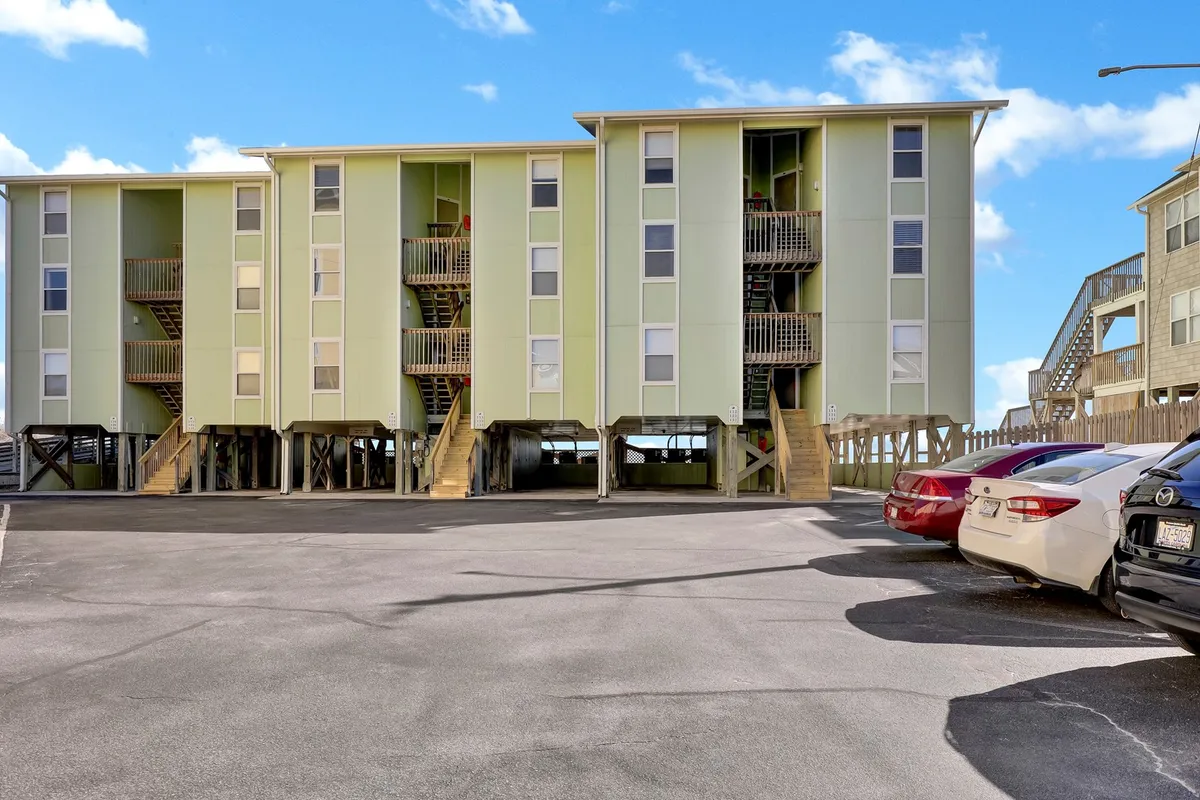 The vibrant, colorful exterior of the condo building, with exterior staircases leading up to the units and a parking area in front. The scene suggests ease of access for families arriving or heading out to explore local attractions.
