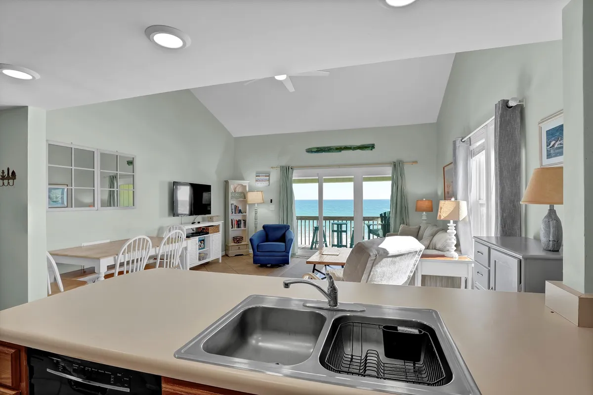 A modern kitchen and dining space opens up to a comfortable living area with large windows revealing spectacular ocean views. The layout encourages flow between cooking, dining, and lounging, with plenty of natural light and a cozy ambiance.