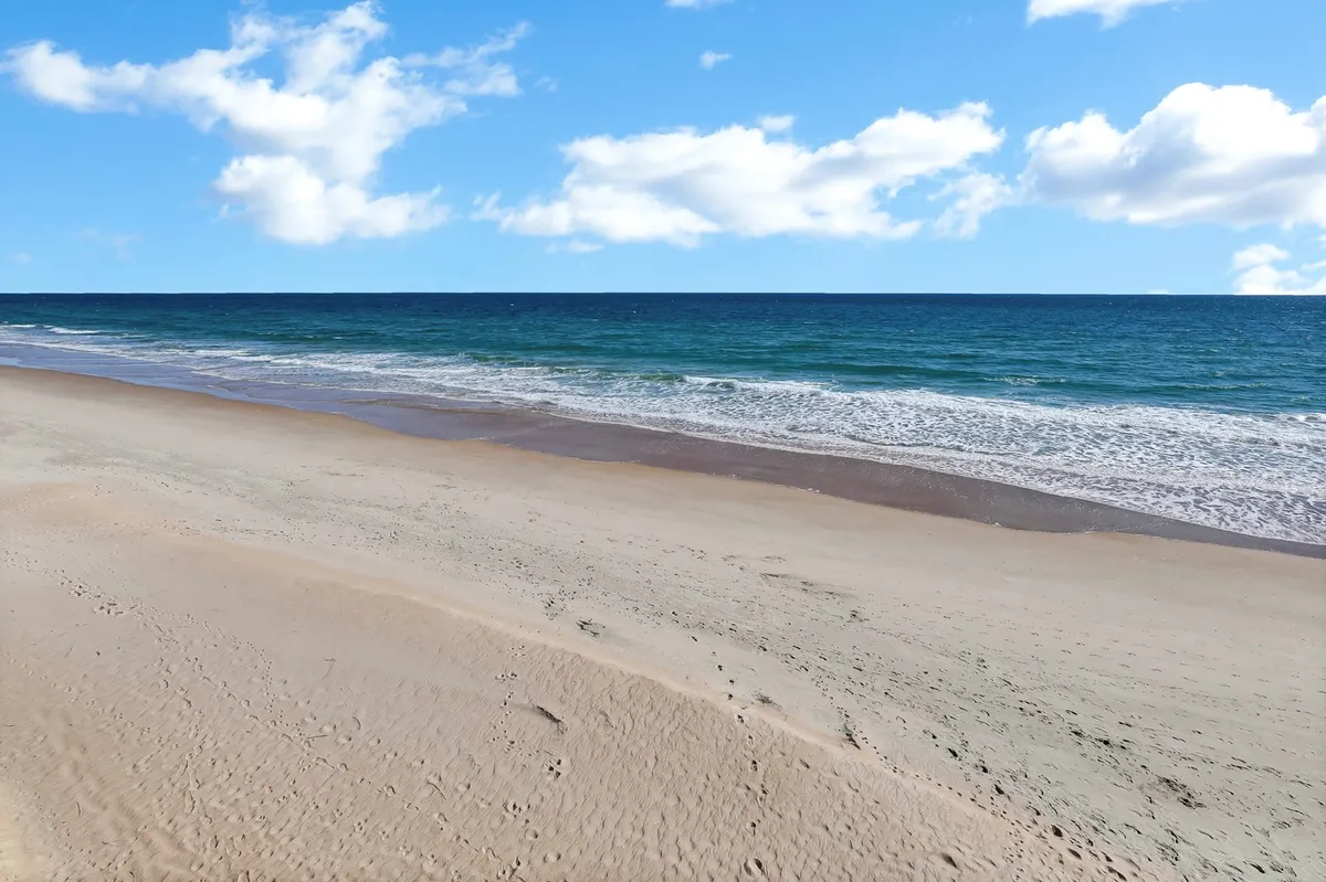 A serene stretch of sandy beach meeting gentle ocean waves under a clear sky. Children and families can be imagined hunting for seashells, building sandcastles, or enjoying a sunrise stroll along the shoreline.